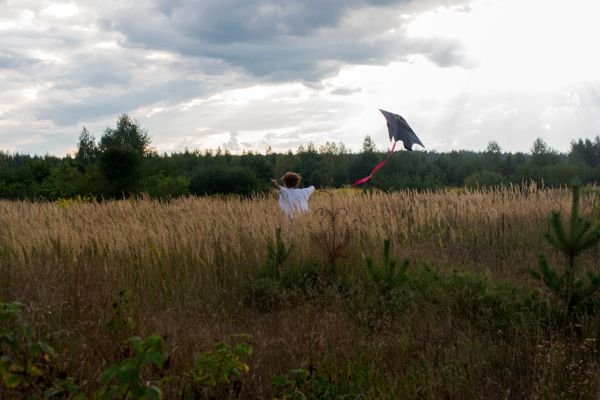 Een kind rent met een vlieger door een grasveld