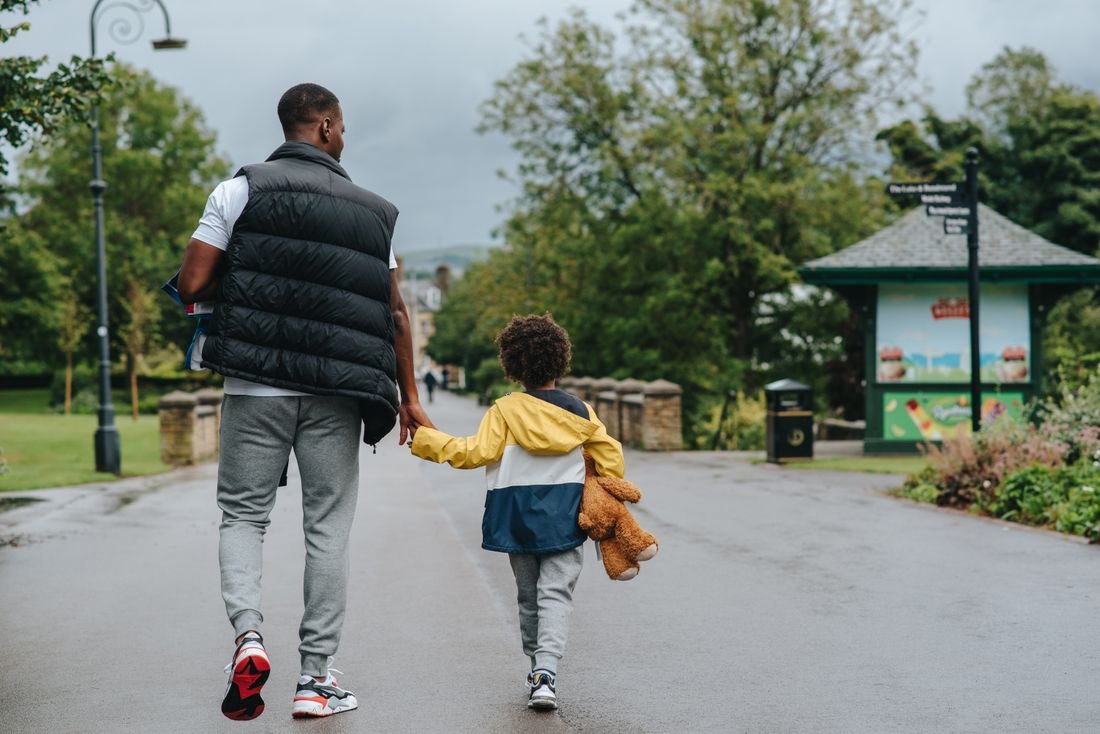 Een volwassene loopt hand in hand met een kind door het park