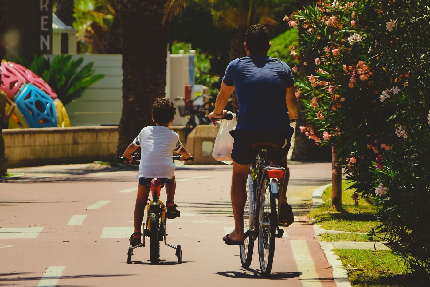 Vader fietst met zijn kind dat leert fietsen met zijwieltjes